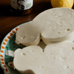 Caciocavallo di bufala tagliato in due all'interno di un piatto decorato con limoni e cime di rapa sullo sfondo.