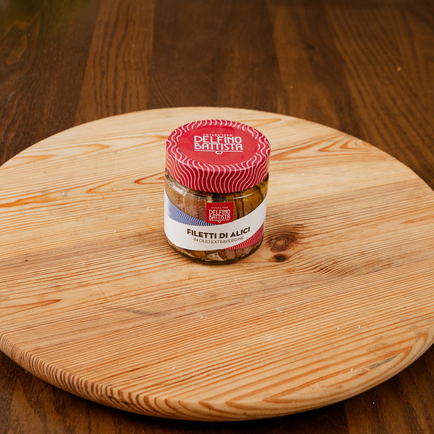 Vasetto di filetti di alici in olio extravergine di oliva su tagiere di legno.