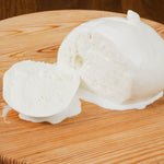 Mozzarella Gigante di latte di Bufala tagliata con latte che gocciola su tagliere di legno.