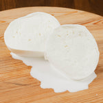 Mozzarella aversana di latte di bufala tagliata con latte che scorre su tagliere di legno.