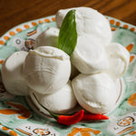 Bocconcini di latte di bufala serviti in piatto decorato, con foglia di basilico e peperoncino rosso fresco.
