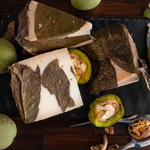 Formaggio caprino avvolto in foglie di noce su tagliere rustico.