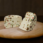 Formaggio fresco di pecora prataiola al peperoncino, rucola e olive tagliato in due su tagliere di legno.