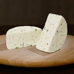 Formaggio fresco di pecora prataiola alla rucola tagliato in due su tagliere di legno.