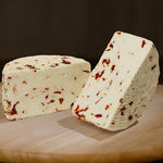 Formaggio fresco di pecora prataiola al peperoncino tagliato in due su tagliere di legno.