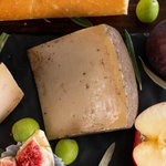 Formaggio caprino stagionato La Sinfonia, affinato con pepe nero e olio extravergine d’oliva, servito con fichi, uva, mela e pane su tagliere rustico.