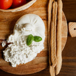 Burrata di bufala tagliata con grissini artigianali e pomodori su tagliere di legno