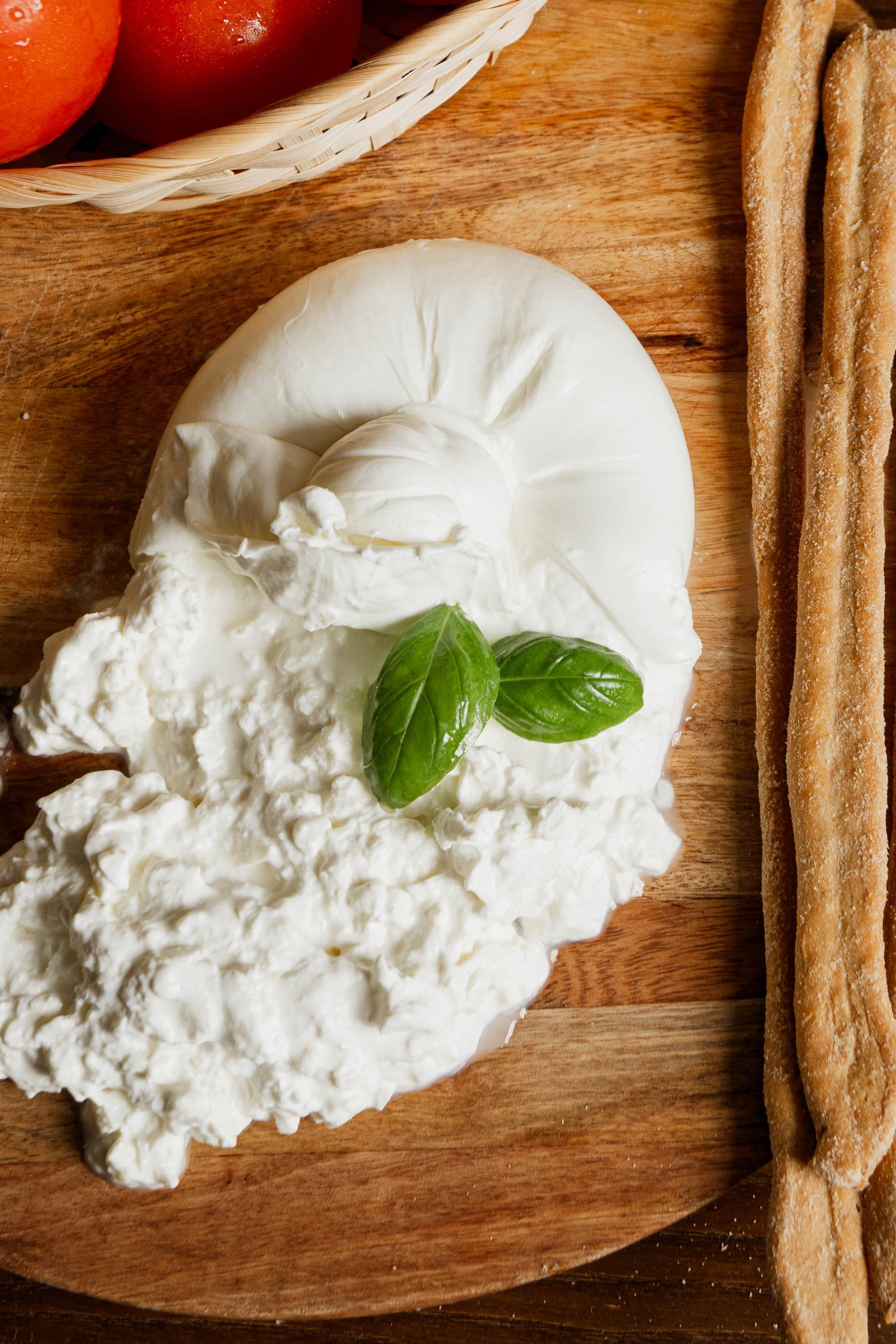 Burrata di bufala tagliata con grissini artigianali e pomodori su tagliere di legno