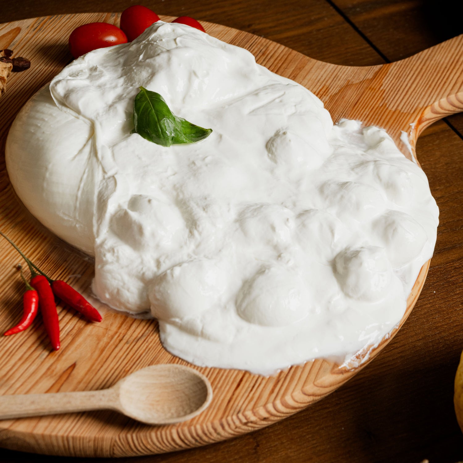 Cucciolata di latte di bufala con panna cremosa e bocconcini, decorata con basilico fresco, servita su tagliere di legno con peperoncini e pomodorini.