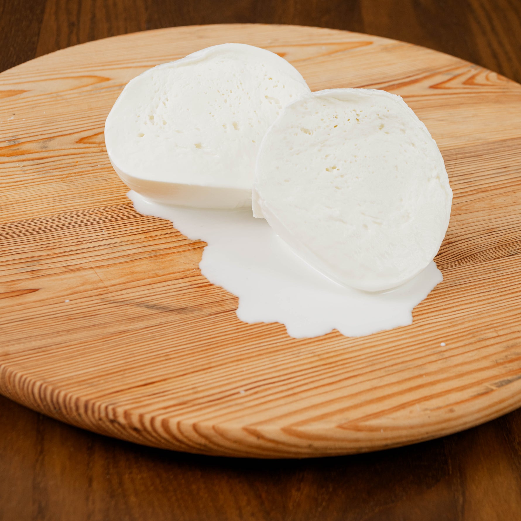 Mozzarella aversana di latte di bufala tagliata con latte che scorre su tagliere di legno.