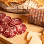 Salamino affettato su tagliere rustico di legno con pane e formaggio