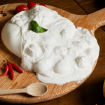 Scrigno di latte di bufala con panna cremosa e bocconcini, decorata con basilico fresco, servita su tagliere di legno con peperoncini e pomodorini.