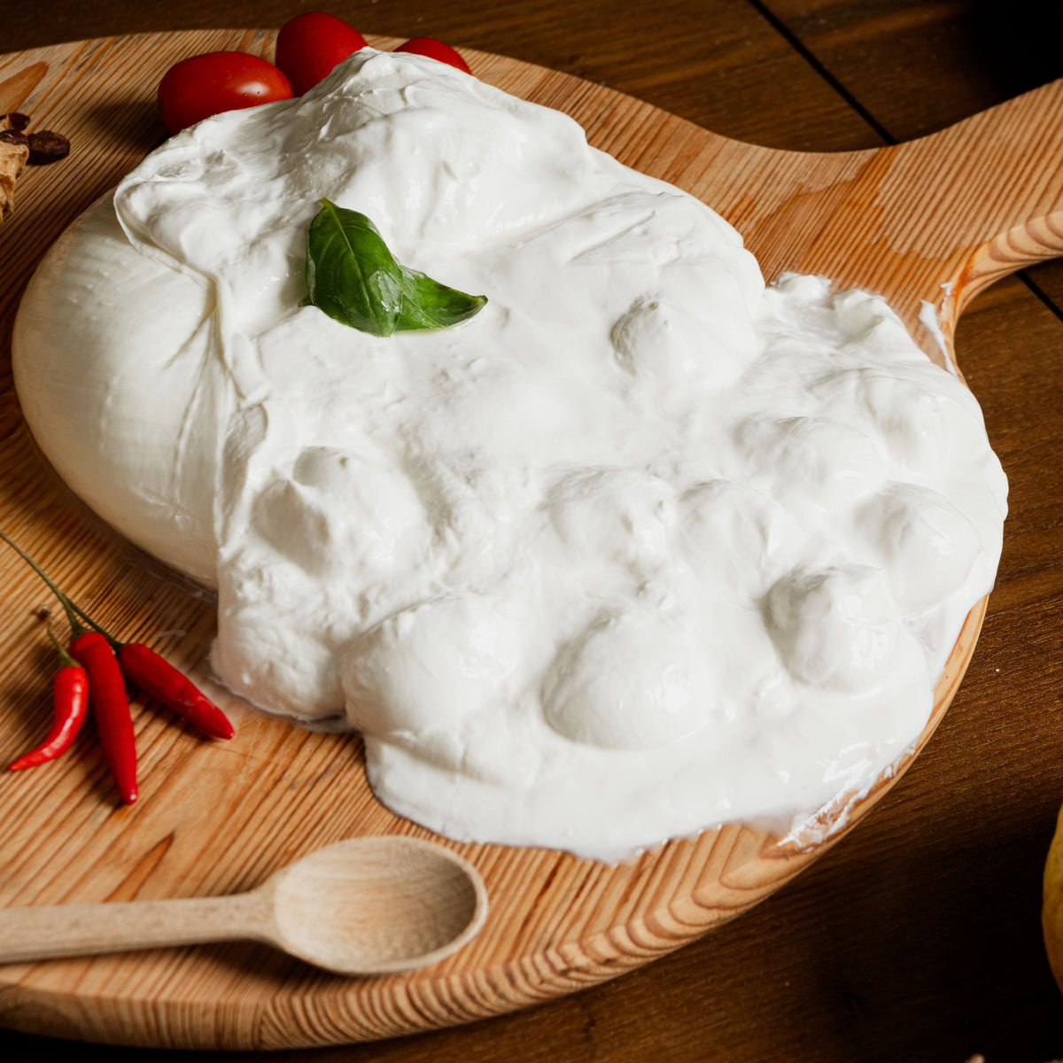 Scrigno di latte di bufala con panna cremosa e bocconcini, decorata con basilico fresco, servita su tagliere di legno con peperoncini e pomodorini.