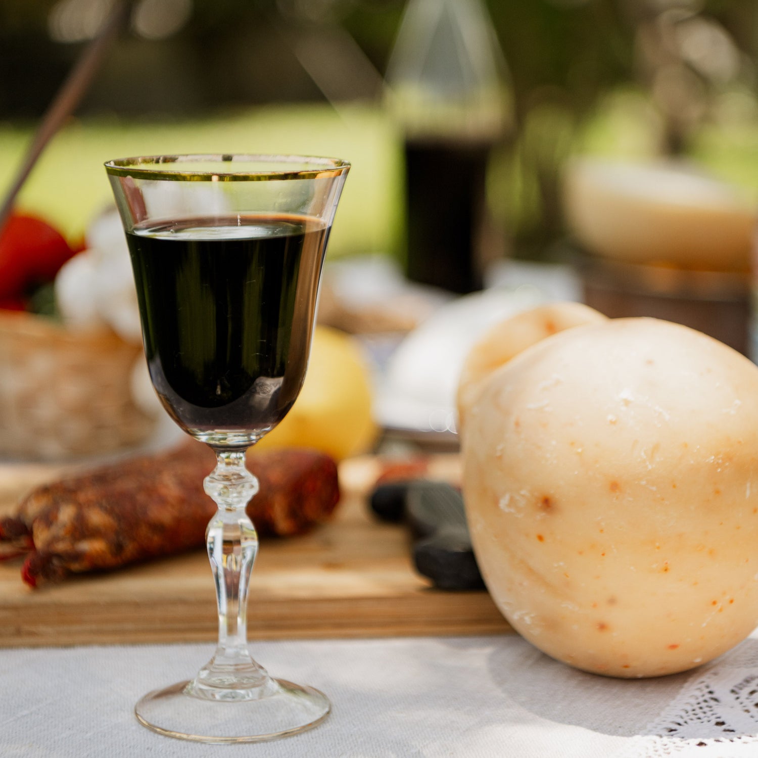 Bicchiere di vino rosso accanto a caciocavallo al peperoncino su tagliere, ideale abbinamento tra formaggio piccante e salumi artigianali.