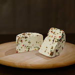 Formaggio fresco di pecora prataiola al peperoncino, rucola e olive tagliato in due su tagliere di legno. 
