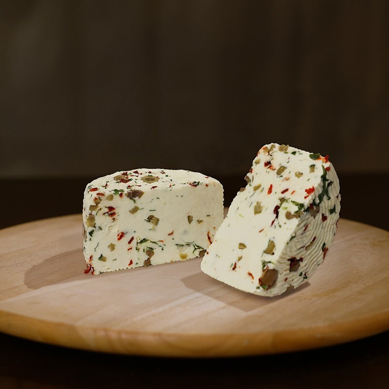 Formaggio fresco di pecora prataiola al peperoncino, rucola e olive tagliato in due su tagliere di legno. 
