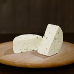 Formaggio fresco di pecora prataiola alla rucola tagliato in due su tagliere di legno.