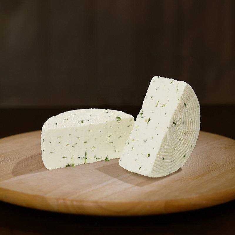 Formaggio fresco di pecora prataiola alla rucola tagliato in due su tagliere di legno.