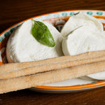 Mozzarella aversana di latte di Bufala  con foglia di basilico e grissini su piatto decorato.