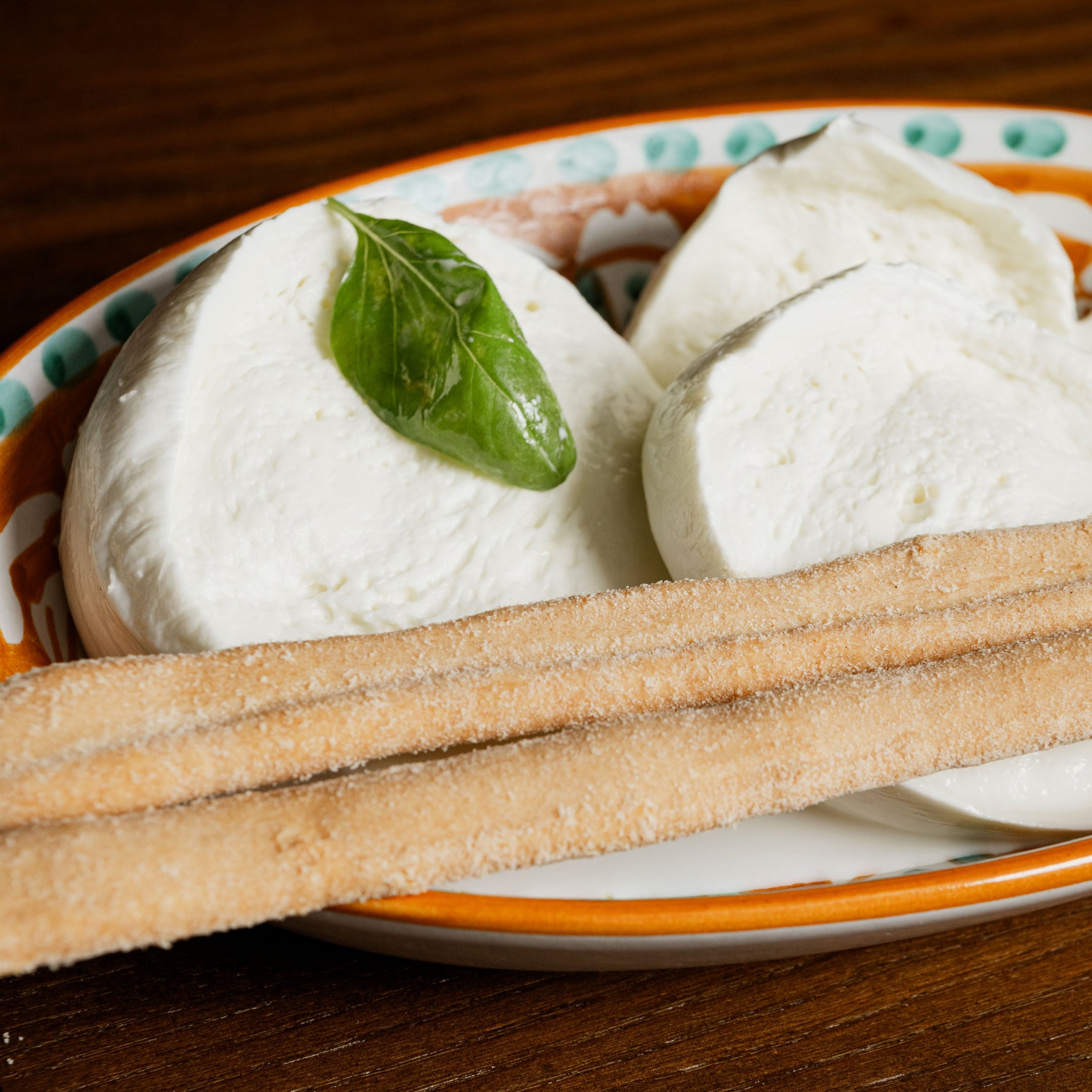 Mozzarella aversana di latte di Bufala  con foglia di basilico e grissini su piatto decorato.