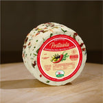 Formaggio fresco di pecora prataiola al peperoncino, rucola e olive su tagliere di legno. 