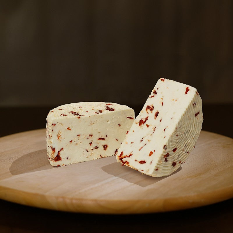 Formaggio fresco di pecora prataiola al peperoncino tagliato in due  su tagliere di legno.