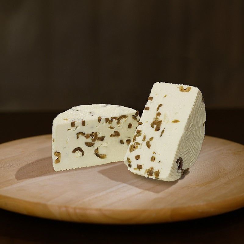 Formaggio fresco di pecora prataiola alle olive tagliato in due su tagliere di legno.