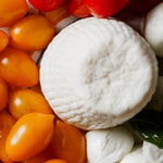 Ricotta dura al centro circondata da pomodori gialli e rossi, bocconcini di mozzarella e foglie di basilico su un piatto colorato