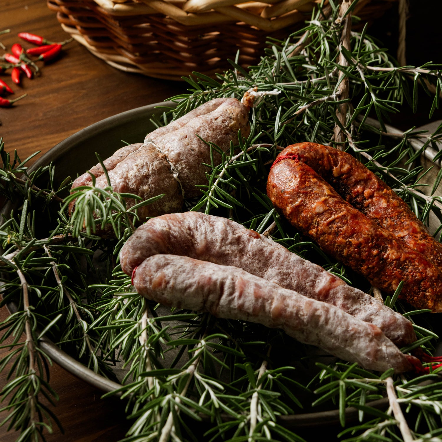 Salsicce cilentane stagionate adagiate su rametti di rosmarino fresco, su tavola rustica in legno.