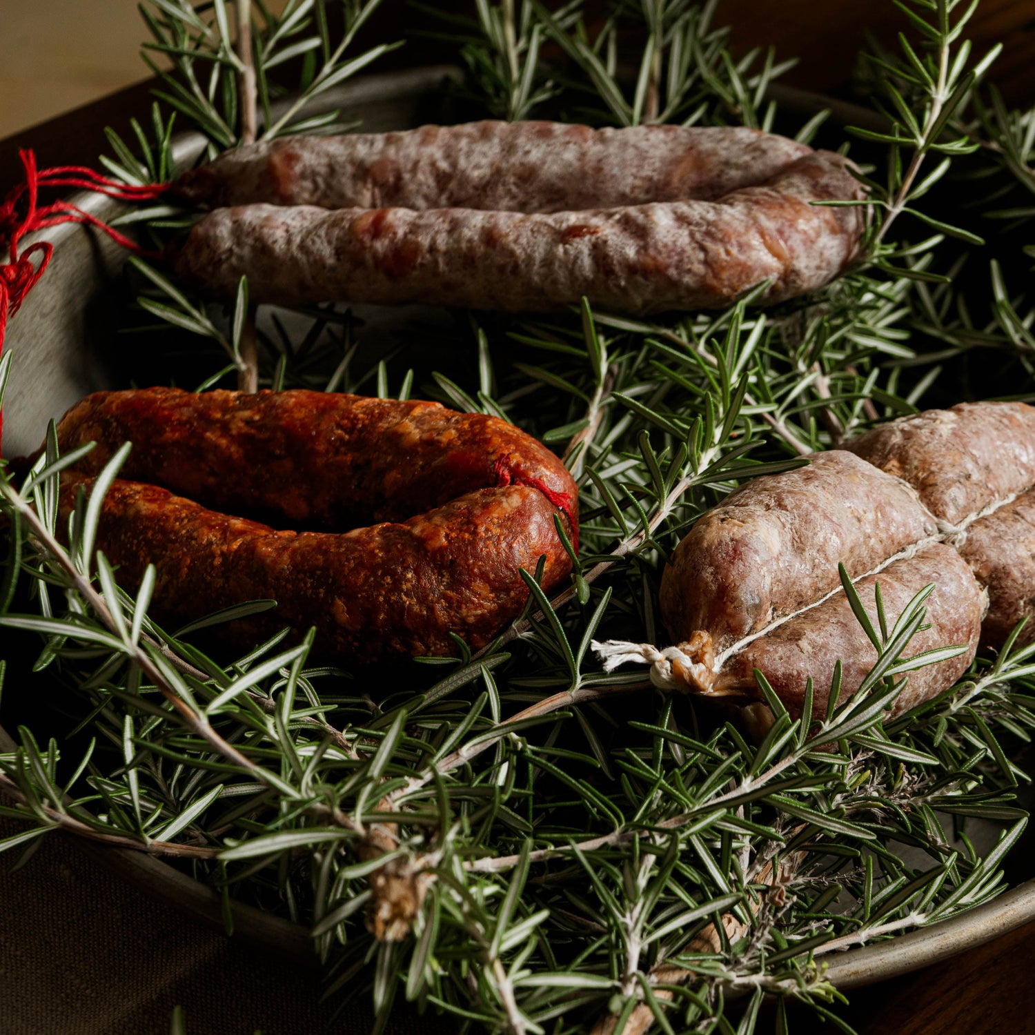 Salsicce stagionate artigianali cilentane adagiate su rametti di rosmarino fresco.