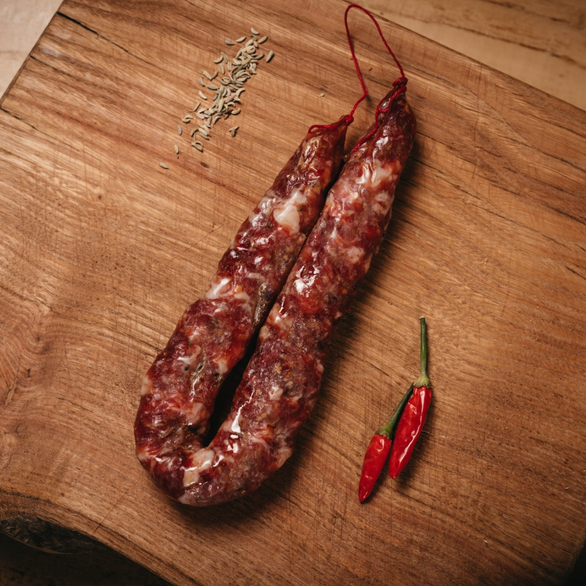 Salsiccia Piccante su tagliere di legno con peperoncino.