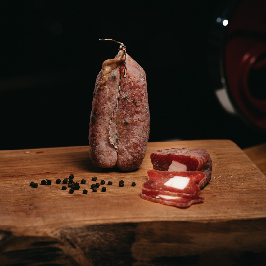 Soppressata Cilentana con Lardello intera e tagliata a fette su tagliere di legno.