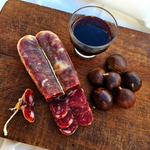 Soppressata cilentana affettata su tagliere rustico con bicchciere di vino e castagne.