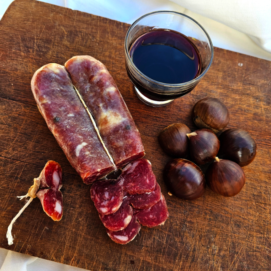 Soppressata cilentana affettata su tagliere rustico con bicchciere di vino e castagne.