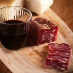 Soppressata affettata su tagliere rustico con un bicchiere di vino.