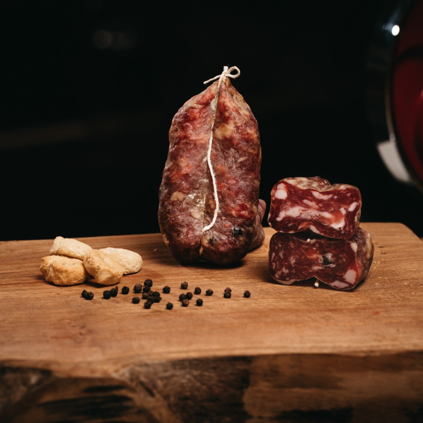Soppressata intera e tagliata su tagliere rustico con taralli e pepe.