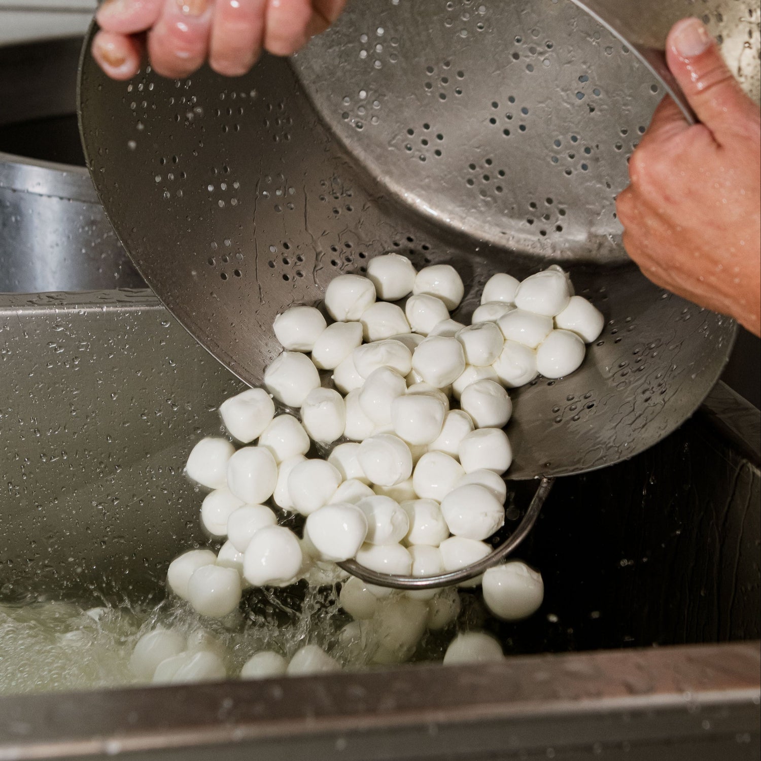 Casaro che versa a mano bocconcini di mozzarella fresca in una vasca di salamoia per il raffreddamento e la conservazione.